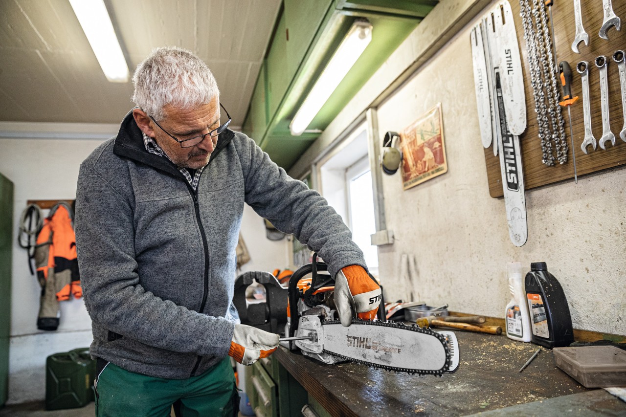 A man in a workshop screwing a STIHL Rollomatic E guide bar onto a chainsaw 