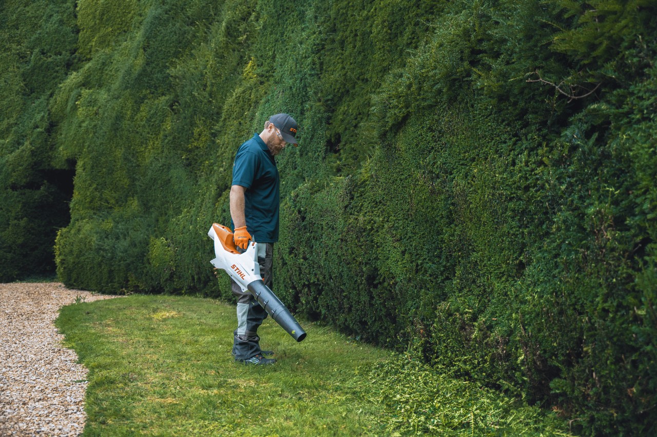 A professional stands in front of the high hedge at Bathurst Estate with a STIHL battery leaf blower