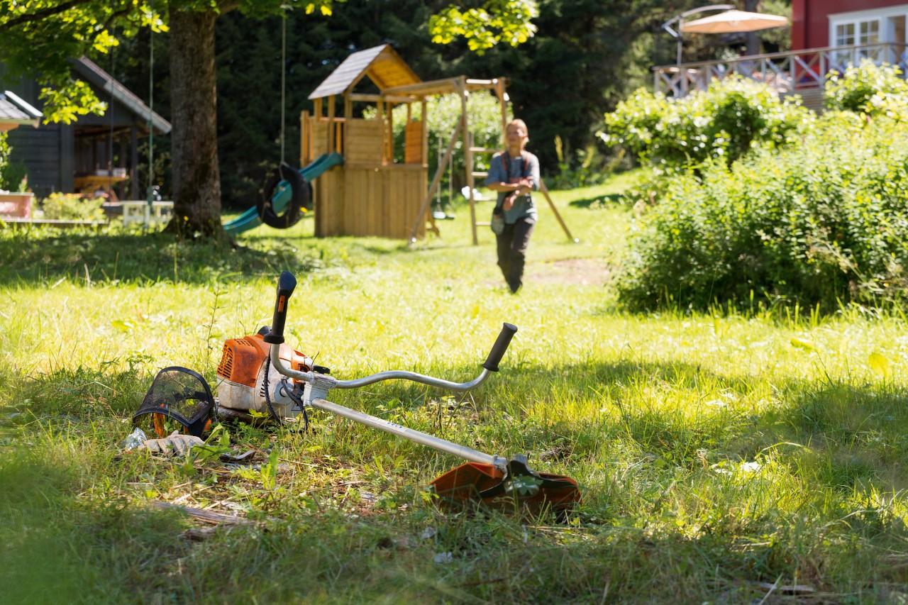 STIHL FS 240 brushcutter in the grass with a man preparing for maintenance in the background
