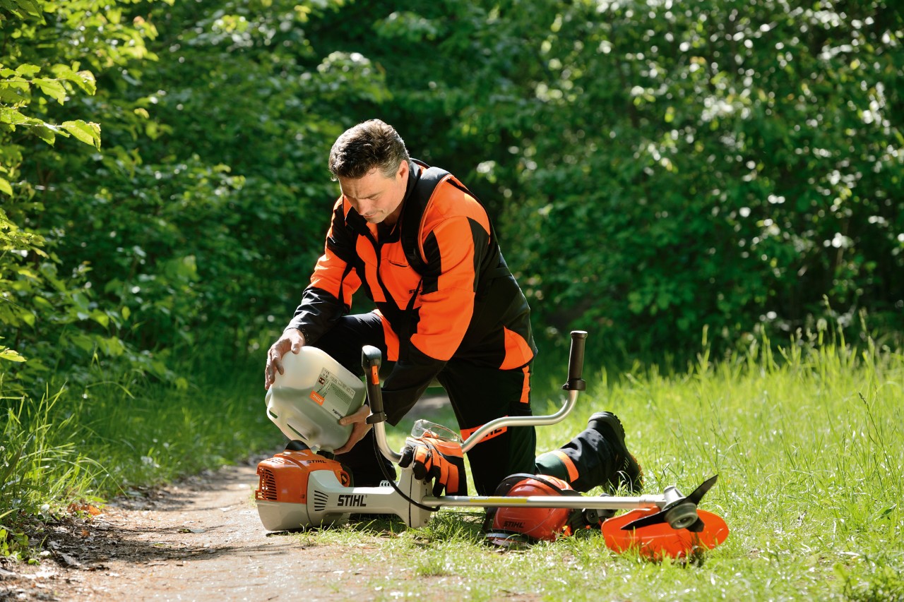 A man wearing STIHL protective equipment refuelling a STIHL brushcutter with a petrol-oil mixture