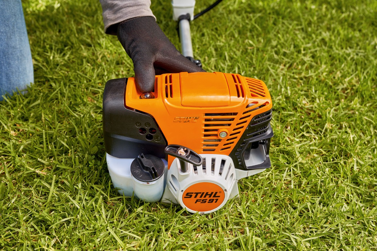 A man pressing the fuel pump of a STIHL FS 91 petrol brushcutter to start it
