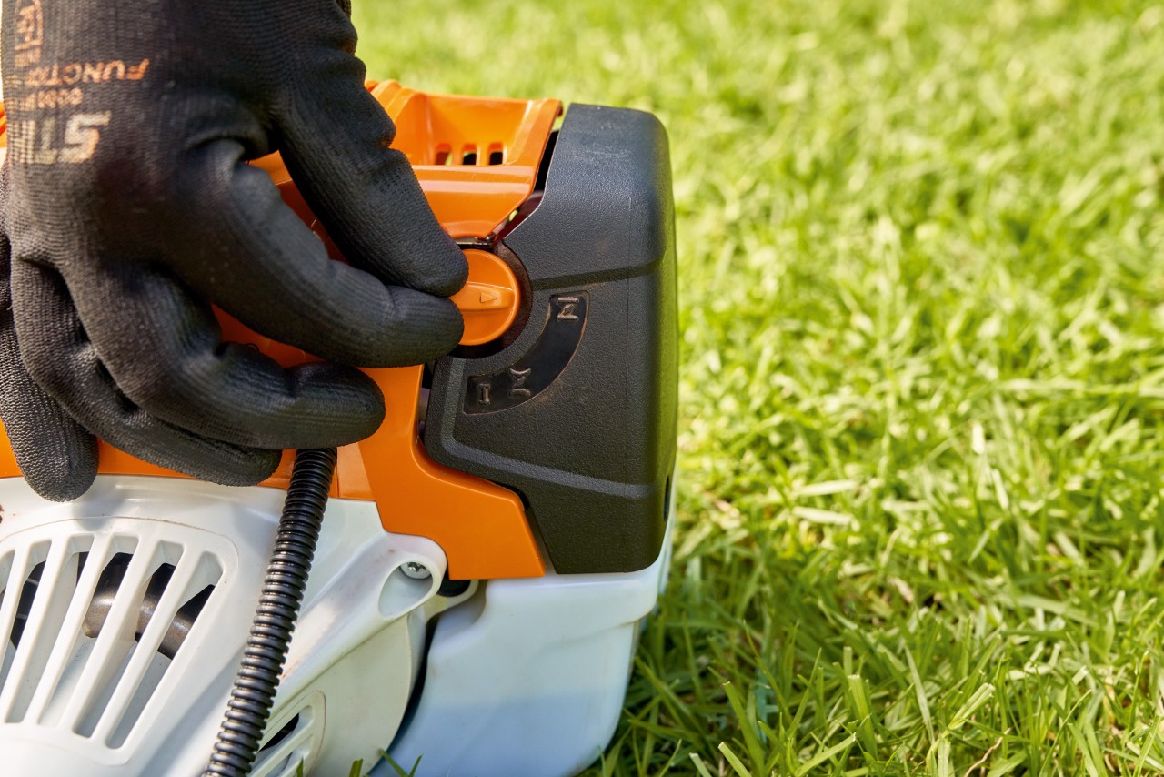 A man adjusting the fuel pump lever of a STIHL FS 91 petrol brushcutter to start it