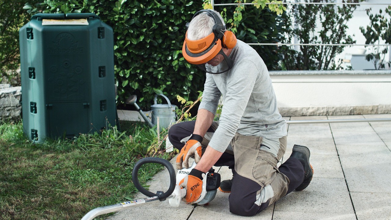 A STIHL FS 38 petrol brushcutter being pressed onto the ground by a person wearing protective clothing
