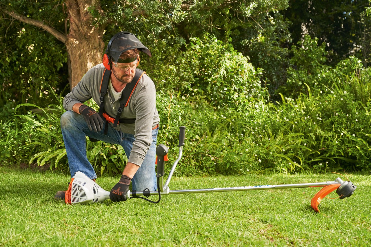 A man placing a STIHL FS 56 petrol brushcutter on the ground to start it