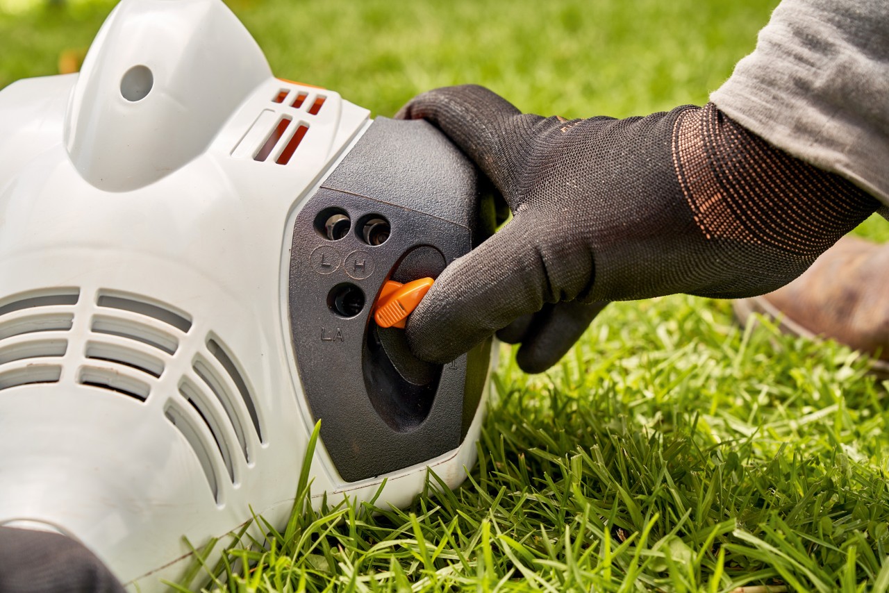 A man adjusting the lever of a STIHL FS 56 petrol brushcutter to start it
