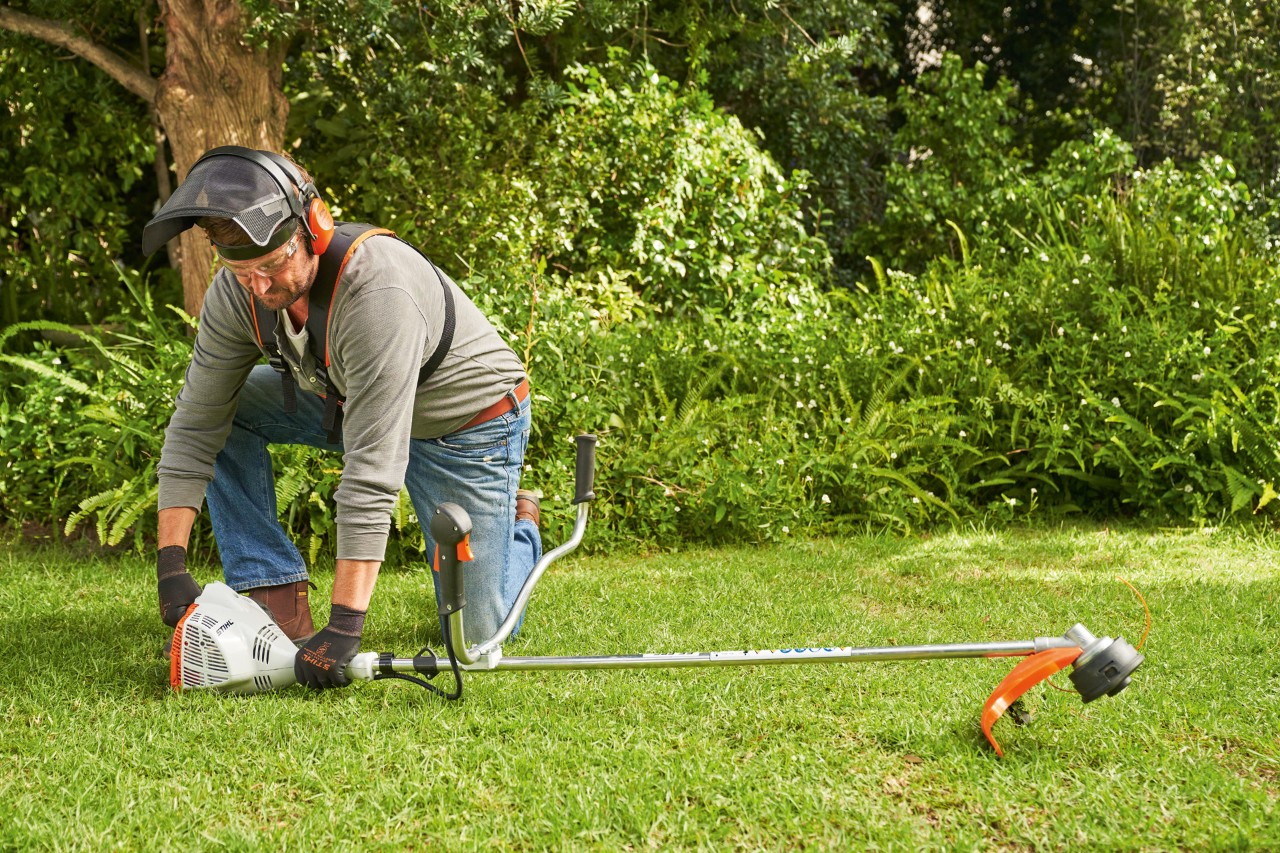 A man pressing a STIHL FS 56 petrol brushcutter firmly onto the ground to start it