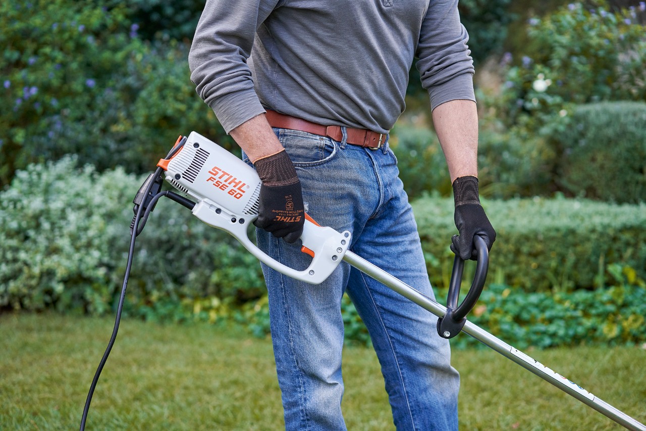 A man wearing protective gloves holding a STIHL FSE 60 electric brushcutter with both hands