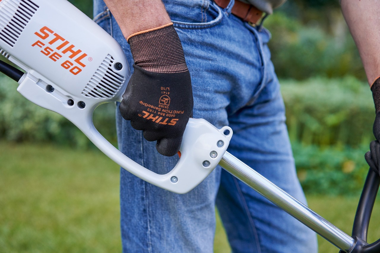Man pressing the switch on the control handle of a STIHL FSE 60 electric brushcutter