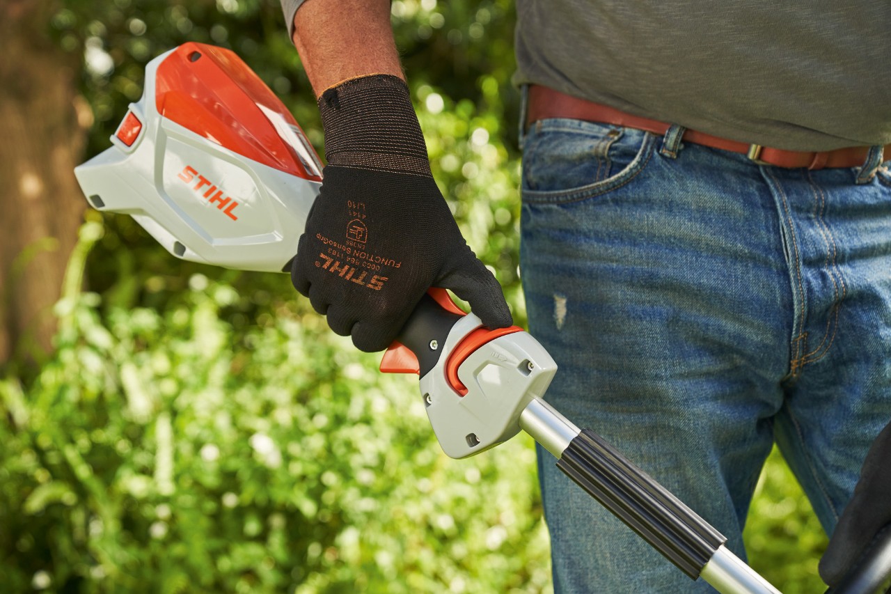 Man wearing protective gloves pushing the release slide of the STIHL FSA 60 cordless brushcutter towards the loop handle