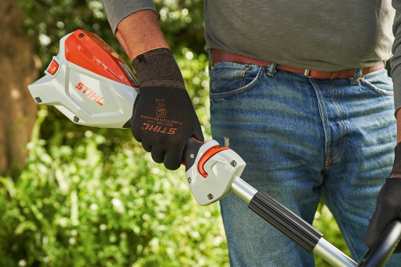 Man wearing protective gloves pressing the trigger of the STIHL FSA 60 cordless brushcutter to start it