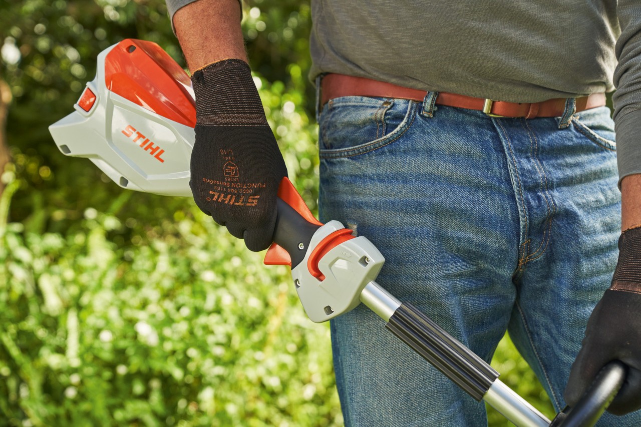 A man wearing protective gloves releasing the trigger of the STIHL FSA 60 cordless brushcutter to switch it off