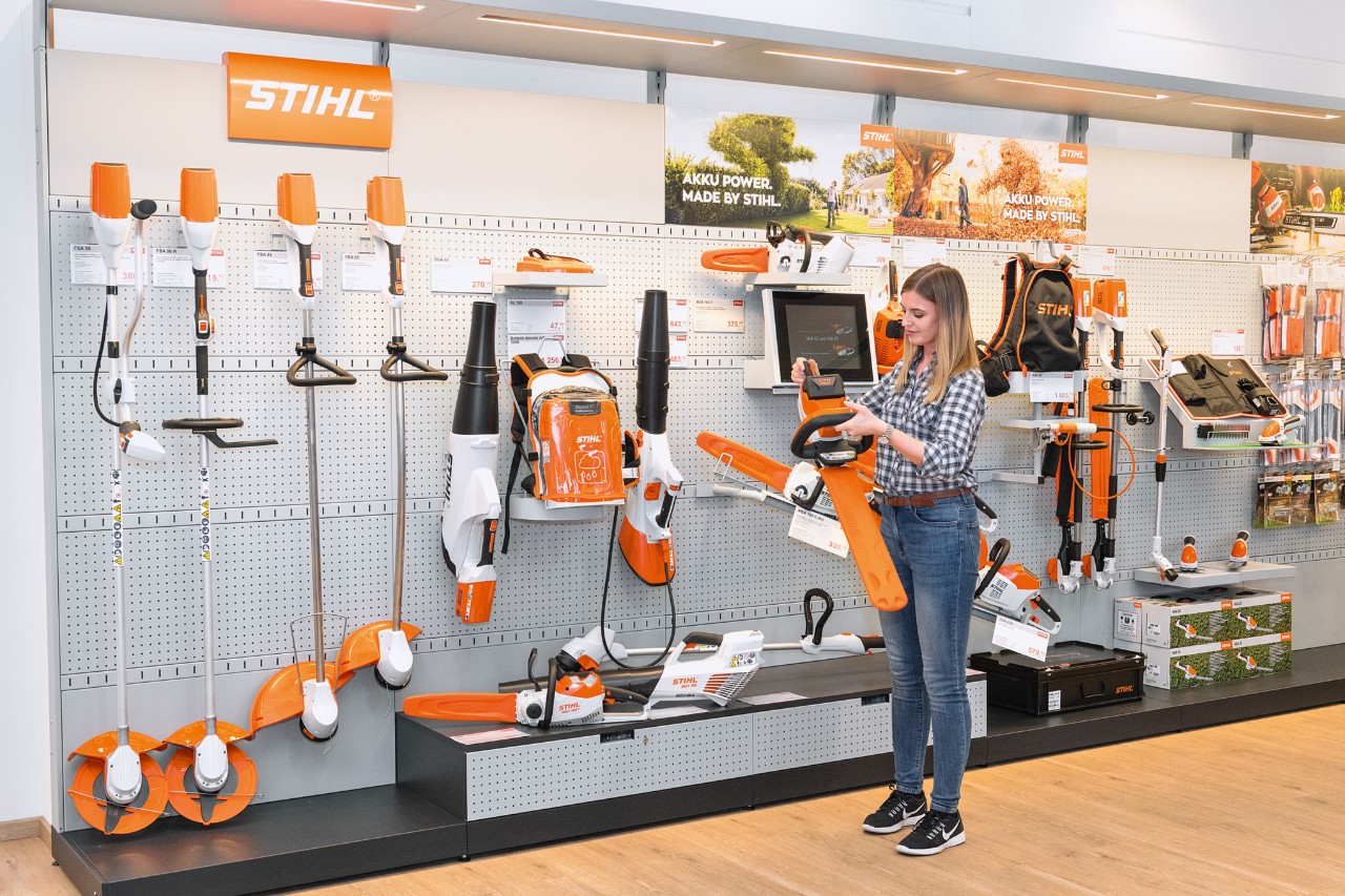 STIHL dealer advising a young woman about a STIHL hedge trimmer in front of a store shelf